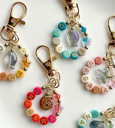 four different key chains with letters and charms attached to them on a white surface,