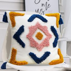 a white pillow with blue, pink and yellow designs on it sitting on a chair