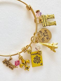 "Perfect souvenir of an enchanting trip to Paris, France. Adjustable gold plated bangle is highlighted with hand stamped quote \"La Vie en Rose\" and 5 detailed Parisian charms accented with rose colored Swarovski crystals AB. Adjustable bangle is made of heavy gold plate over 1.8mm stainless steel. It is hypoallergenic and tarnish resistant. The diameter is 2 1/2\" to fit most. Hand stamped 5/8\" 24 gauge shiny brass disc reads \"La Vie en Rose\". Two 6mm rose colored Swarovski crystals AB and Gold Charm Bracelet As A Souvenir, Personalized Bracelet Jewelry As Souvenir, Personalized Bracelet Jewelry Souvenir, Personalized Bracelet Jewelry For Souvenir, Gold Charm Bracelet For Friendship And Mother's Day, Handmade Gold Charm Bracelet For Mother's Day, Pink Jewelry With Charms For Personalized Gift, Adjustable Pink Gold Charm Bracelet For Gift, Adjustable Charms Jewelry Souvenir