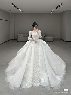 a woman in a white wedding dress holding a cell phone up to her face while standing in an empty room