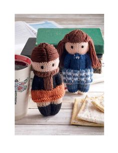 two knitted dolls sitting next to each other near a cup of coffee and cookies