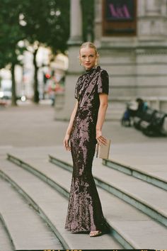 a woman is standing on some steps wearing a long black dress and holding a purse