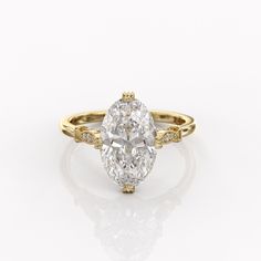 an oval cut diamond ring with yellow gold accents on the shoulders and sides, set against a white background