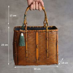 a person's hand holding a brown wicker purse with tassels on it