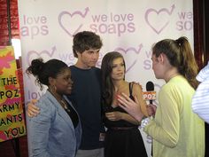 three young people are talking to each other in front of a sign that says we love soaps