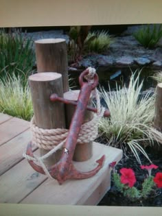 an anchor and rope sitting on top of a wooden post in front of some flowers