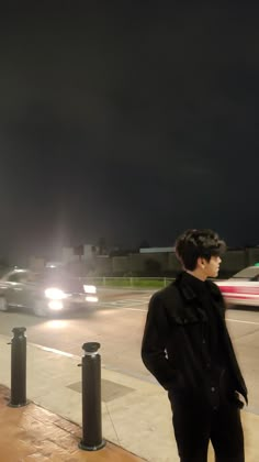 a young man standing on the side of a road at night with his hands in his pockets