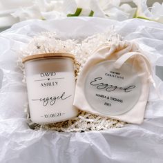 two personalized candles in a gift box with white flowers behind them and a heart shaped tag on the lid