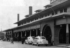 an old black and white photo of cars parked in front of a building with people standing outside