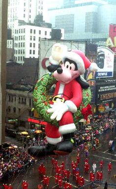 an inflatable santa clause balloon floats down a city street as people watch from the sidelines