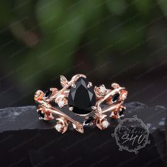 a black diamond ring sitting on top of a stone slab in front of a green leafy background