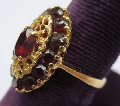 This ring looks so regal! The deep red garnets against the rich colored 18k gold compliment each other beautifully. Dating from the early 1900's-40's and hallmarked in the interior 750 and 176AAL. Has been tested to ensure the golds purity. Rings size is 6 1/2 and is ready to be worn and admired! The halo setting measures 11/16 by 7/16 of an inch. Stones are all held securely in place. Center garnet measures 6.12mm by 4.25mm. Some stones have light surface wear as to be expected with a ring of s Elegant Garnet Ruby Ring Stamped 14k, Vintage Red Garnet Cluster Ring, Victorian Ruby Rings In Yellow Gold, Victorian Ruby Ring In Yellow Gold, Victorian Yellow Gold Rings With Ruby, Vintage Ruby Cluster Ring For Formal Occasions, Vintage Ruby Cluster Ring For Formal Events, Formal Gold Rings With Garnet, Heirloom Oval Garnet Cluster Ring