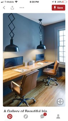 a desk with two computers on it in front of a window and some lights hanging from the ceiling