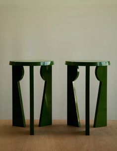 two green tables sitting next to each other on a wooden floor in front of a white wall