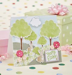 an easter card with trees and flowers on it, next to a gift box that says happy easter