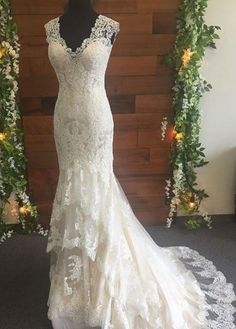 a wedding dress is displayed on a mannequin in front of a wall with greenery