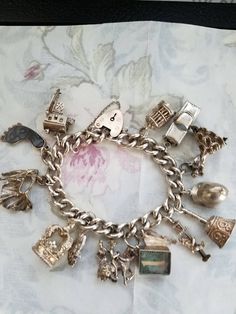 "This is a beautiful sterling silver charm bracelet.  It comes with a vintage English heart lock closure and a nice solid link bracelet. It has the English markings on the back of the lock. The charms are as follows: 1). An Irish cottage with a spinning wheel inside. 2}. \"Hang Ten\" foot charm with abalone shell. 3). A bull fighter with cape. 4}. Large English Queen's crown. 5). A Scottish man in kilt 6). Spanish woman and man on horse (horse leg missing) 7). One pound inside locket it is engra Vintage Sterling Silver Charms Jewelry, Antique Sterling Silver Charm Bracelets, Antique Sterling Silver Bracelets With Charms, Silver Vintage Charm Classic Jewelry, Classic Collectible Charms Jewelry, Vintage Silver Charm Bracelet As Gift, Classic Charm Bracelet With Vintage Charm As Gift, Vintage Sterling Silver Charm Bracelet As Gift, Vintage Engraved Charm Bracelet Gift