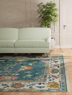 a green couch sitting on top of a wooden floor next to a white chair and potted plant