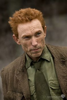 a man with red hair wearing a green shirt and tie is looking at the camera