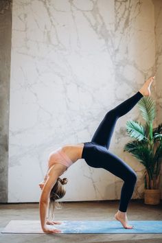 a woman doing a handstand on a yoga mat in front of a plant