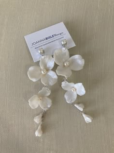 three white orchids with pearls hanging from the end of each earring, on a beige background