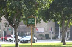 a street sign sitting in the middle of a park next to some trees and cars