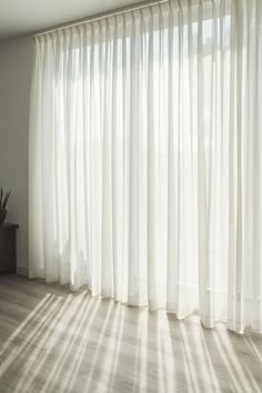 the sun is shining through the curtains in this room with wood flooring and large windows