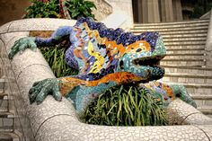 a colorful lizard statue sitting on top of a stone bench next to some steps and plants