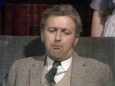 a man wearing a suit and tie sitting in a chair with his eyes closed while looking off to the side