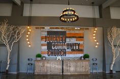 an empty church with trees and lights hanging from the ceiling in front of a sign that reads, journey community church