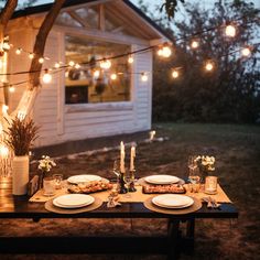 a table set for dinner outside with lights strung over it and plates on the table