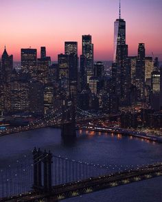 the city skyline is lit up at night with skyscrapers in the foreground and bridge to the right