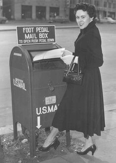 a woman standing next to a mailbox with a us postal sign on it's side