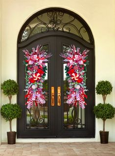 two wreaths on the front door of a house with potted plants and trees