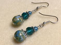 two blue and green glass beaded earrings on silver earwires sitting on a white surface