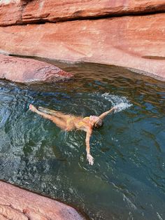 a man is swimming in the water near some large rocks and red rock formations,