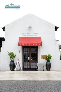 a white building with red awnings and black planters in front of it