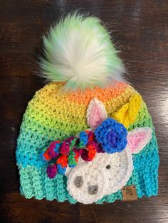 a crocheted hat with a rainbow horse on it and a white pom - pom