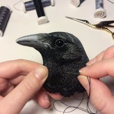 a black bird is being stitched on to a piece of fabric by someone's hands