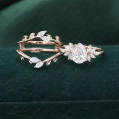 two wedding rings with leaves and diamonds on top of a green velvet surface, close up