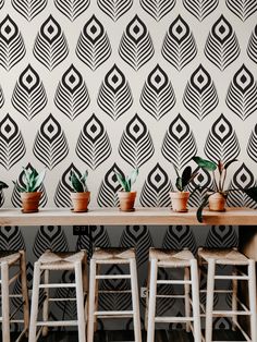 several potted plants sit on stools in front of a wall with black and white designs