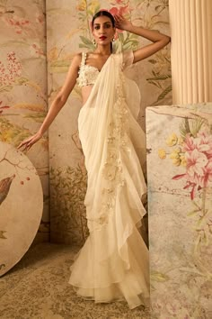 a woman in a white sari standing next to a wall with flowers on it