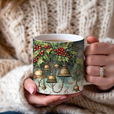 a woman is holding a coffee mug with bells on the front and holly decorations on the outside