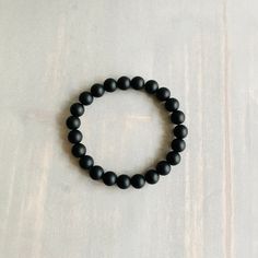 "DETAILS:  8mm Matte Black Onyx beaded bracelet on clear elastic stretch cord. A smooth matte finish gives the bracelet a sleek modern look. It is a unisex bracelet making it a good choice for men, women, and teens.  SIZE: Add .75\" - 1.0\" inch to your wrist measurement.  DESCRIPTION: Whether you are looking for a statement piece or a subtle addition to your collection, this bracelet is a great choice. It is a minimalist-style unisex stretch bracelet making it a good choice for men, women, and Black Onyx Stretch Bracelet With 8mm Beads, Black Onyx 8mm Beads Stretch Bracelet, Minimalist Onyx Beaded Bracelets With Round Beads, Minimalist Onyx Beaded Bracelet With Round Beads, Minimalist Onyx Beaded Bracelet, Adjustable Black Wristband With 8mm Beads, Adjustable Black Wristband With Round Beads, Classic Adjustable Black Bead Bracelets, Classic Onyx Beaded Bracelets With Adjustable Fit