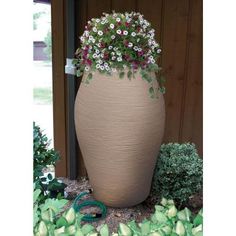 a large planter with flowers in it sitting on the ground next to some bushes