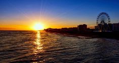 the sun is setting over the ocean with a ferris wheel in the distance