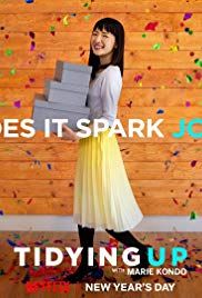 a woman holding a stack of boxes in front of a wooden wall with confetti on it