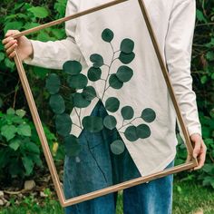 a man is holding a framed photo with leaves on it