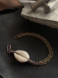 This beautiful cowrie shell is wire wrapped with pure organic copper.  The chain is vintage stock and made of solid brass.  The metals have been oxidized for a rustic / tribal feel.  All jewelry from my studio is endowed with a lifetime craftsmanship guarantee & arrives attractively packaged and ready for gifting or keeps. MEASUREMENTS & SPECIFICS:LENGTH: 7.25" can be adjusted upon requestMETAL: solid vintage brass chain w/ hand forged copper hook / wire wrappingGEMSTONE: cowrie shell se Bohemian Brass Bracelets With Adjustable Chain, Bohemian Handmade Shell-shaped Bracelets, Handmade Metal Bracelets For Beach, Nickel Free Bohemian Shell Jewelry, Bohemian Shell-shaped Nickel-free Jewelry, Bohemian Shell Bracelet, Bohemian Nickel-free Shell Jewelry, Adjustable Shell Jewelry Nickel Free, Handmade Vintage Bracelets For Beach