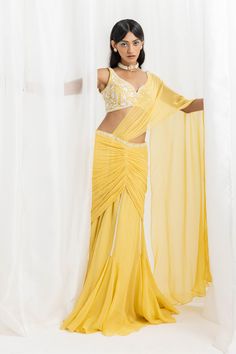 Editor's Note A yellow embellished choli paired with an embellished pre-stitched flared sari and blouse would make for a stunning outfit. You can accessorize with statement jewelry and a clutch to complete the look. Fabric: Blouse: georgette, sari: georgette and organza, lining: satin Color: Yellow Components: Sari and blouse Occasion: Cocktail, haldi mehndi and Wedding Guest Disclaimer: Product color may slightly vary due to photographic lighting sources or your monitor setting. Care: Dry clean Designer Pre-draped Yellow Saree, Draped Sharara With Mirror Work For Diwali, Diwali Sharara With Mirror Work And Draped Style, Festive Yellow Pre-draped Saree With Mirror Work, Yellow Pre-draped Designer Saree, Draped Lehenga With Mirror Work In Georgette, Yellow Designer Wear Pre-draped Saree, Bollywood Style Draped Georgette Lehenga, Bollywood Style Draped Georgette Choli